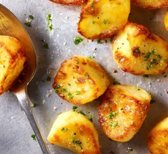 Roast potatoes served on a baking tray with herbs